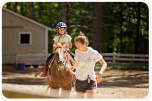 A counselor leads a young girl on a walk around our riding ring.