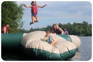 A camper leaps into the air to send a color-wars teammate flying off our water trampoline's blob.